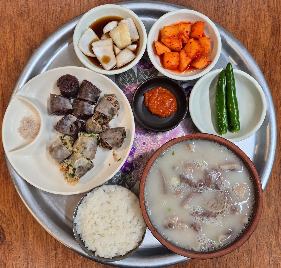 둥근 쟁반에 차린 한 상 — 국밥, 공기밥, 순대와 소금, 깍두기, 간장 절임 채소, 다대기, 풋고추 두 개